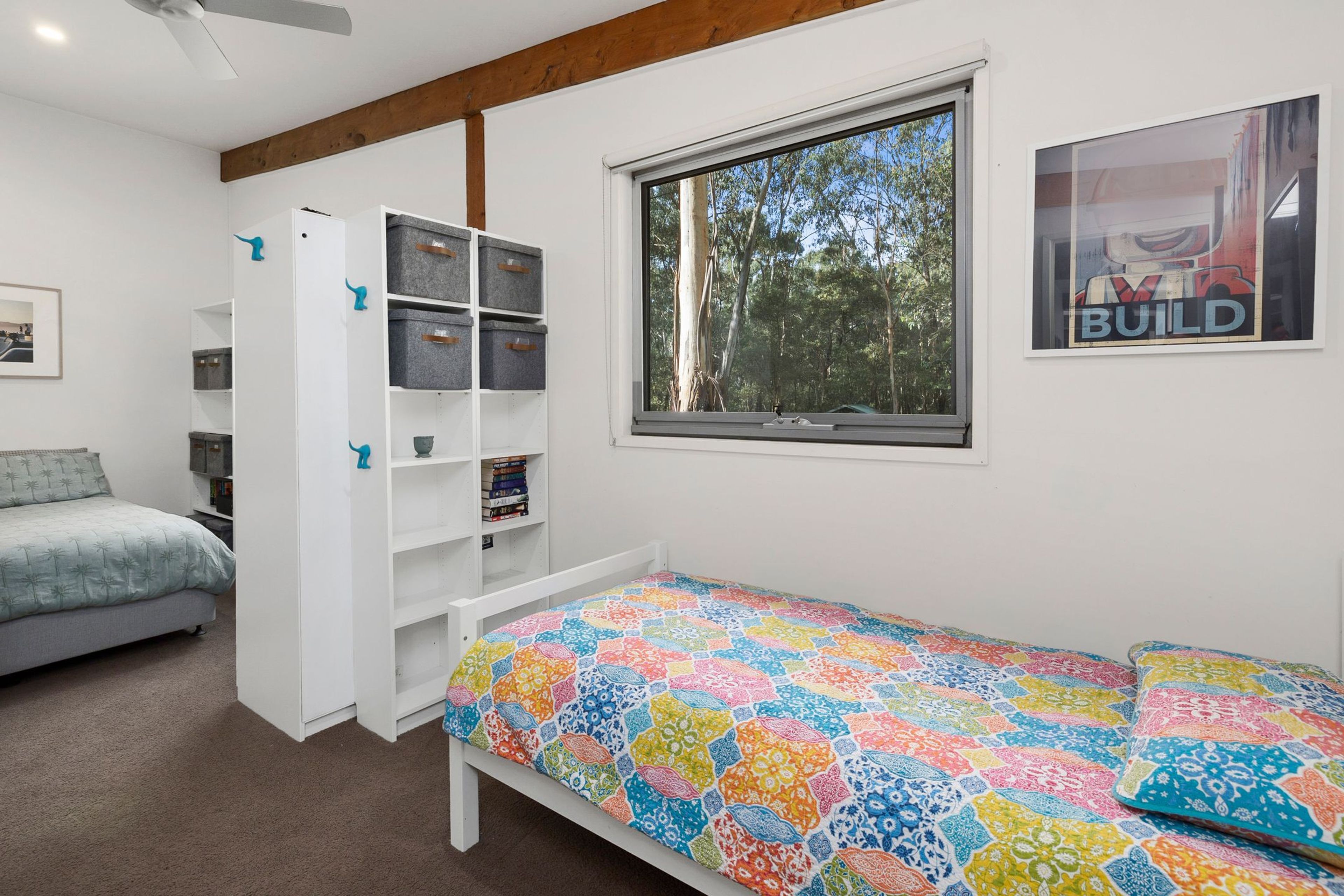 A bedroom with a bed, a built-in wardrobe, a window with a view of trees, and a poster on the wall.
