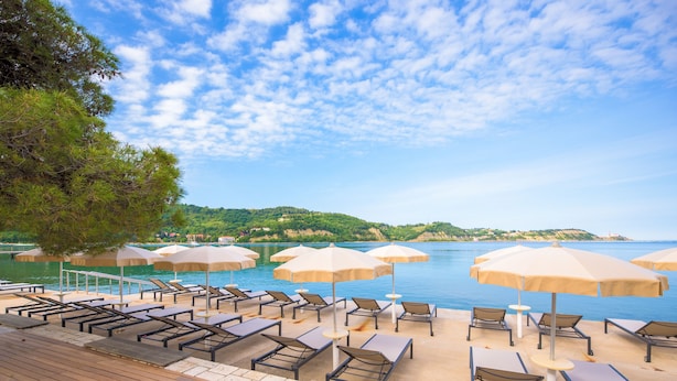 A beachside lounge area with sun loungers and umbrellas, overlooking a body of water and a hilly landscape. - Vila Laguna Strunjan (Piran)