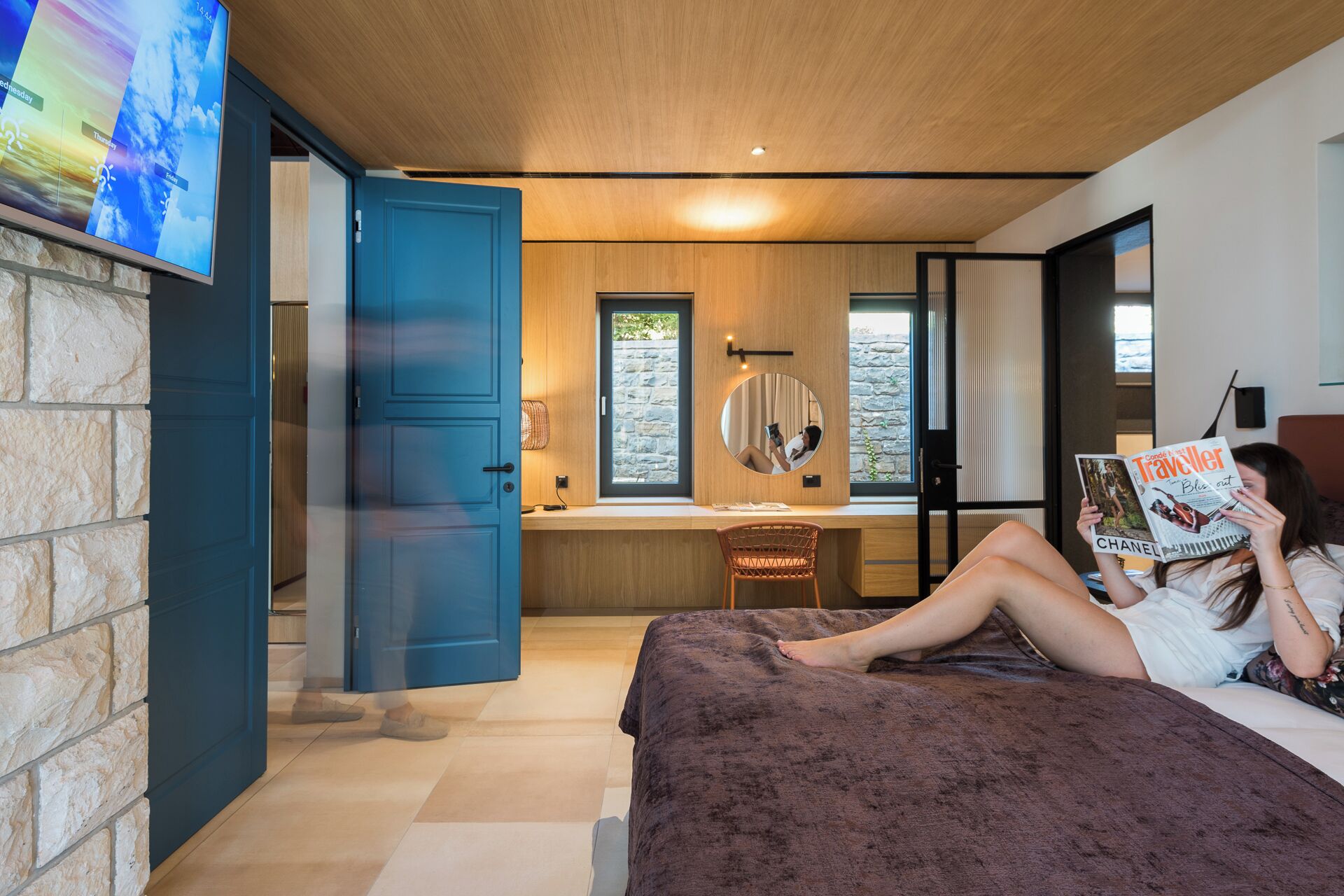 Une chambre à coucher moderne avec un lit, un fauteuil de lecture, un bureau et un grand miroir.