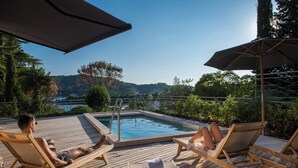 A wooden deck with a pool, lounge chairs, and a view of a lake and hills. - Vila Laguna Strunjan (Piran)
