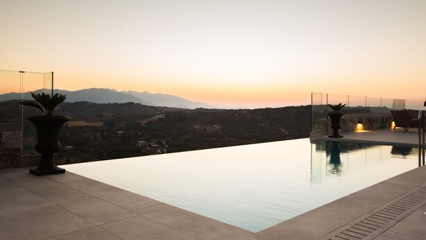 En infinitypool med utsikt över bergen vid solnedgången.