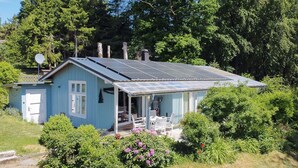 Et lille, etetages hus med solpaneler på taget, en veranda med udendørs møbler, og en have med forskellige planter og blomster.