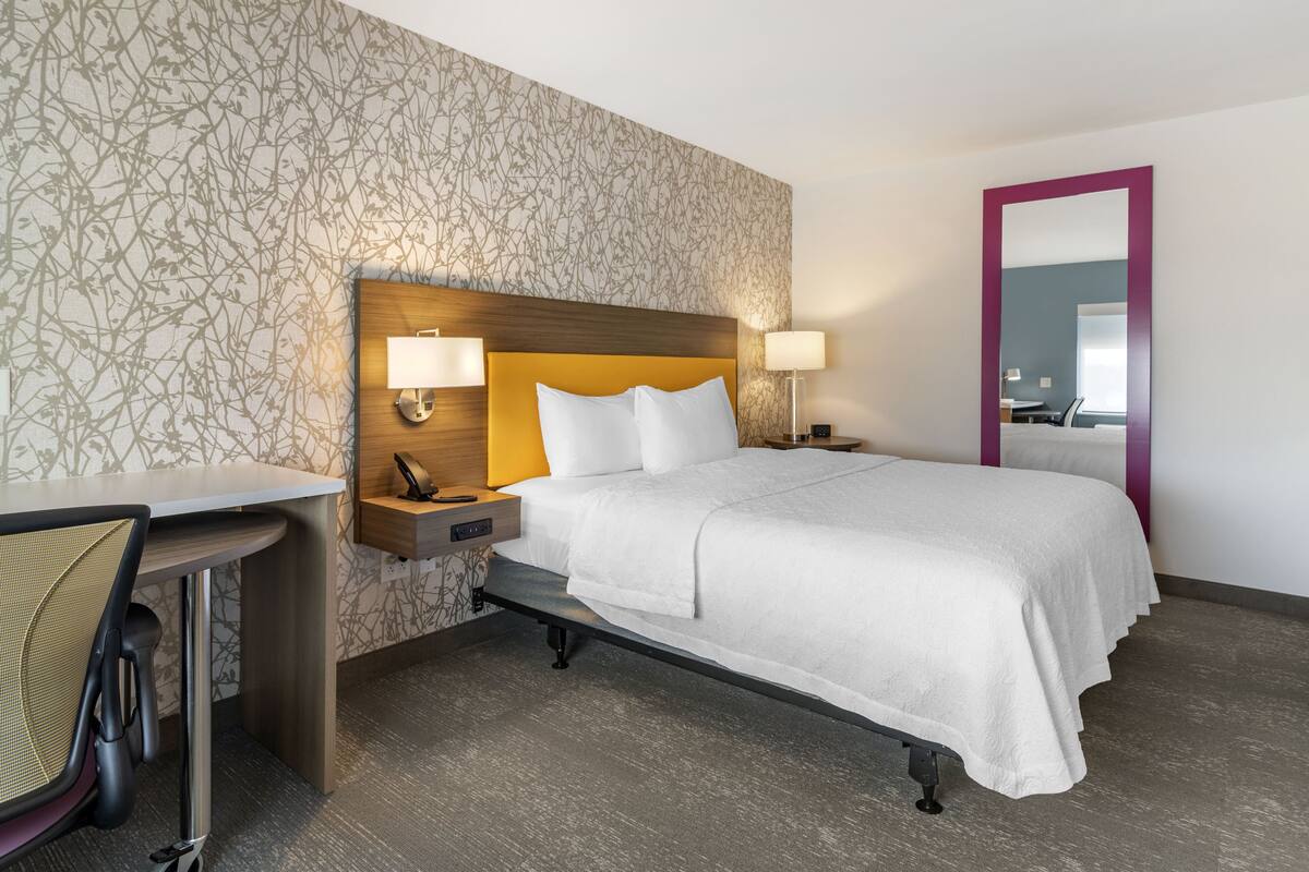 A hotel room with a bed, bedside tables, a desk, and a chair.
