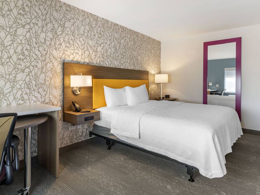 Quarto de hotel com cama, mesas de cabeceira, escrivaninha e uma cadeira.