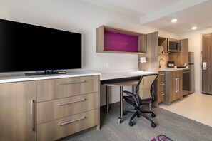 A modern kitchen with a flat-screen TV, wooden cabinets, and a built-in microwave. - Home2 Suites by Hilton Bangor (Bangor)
