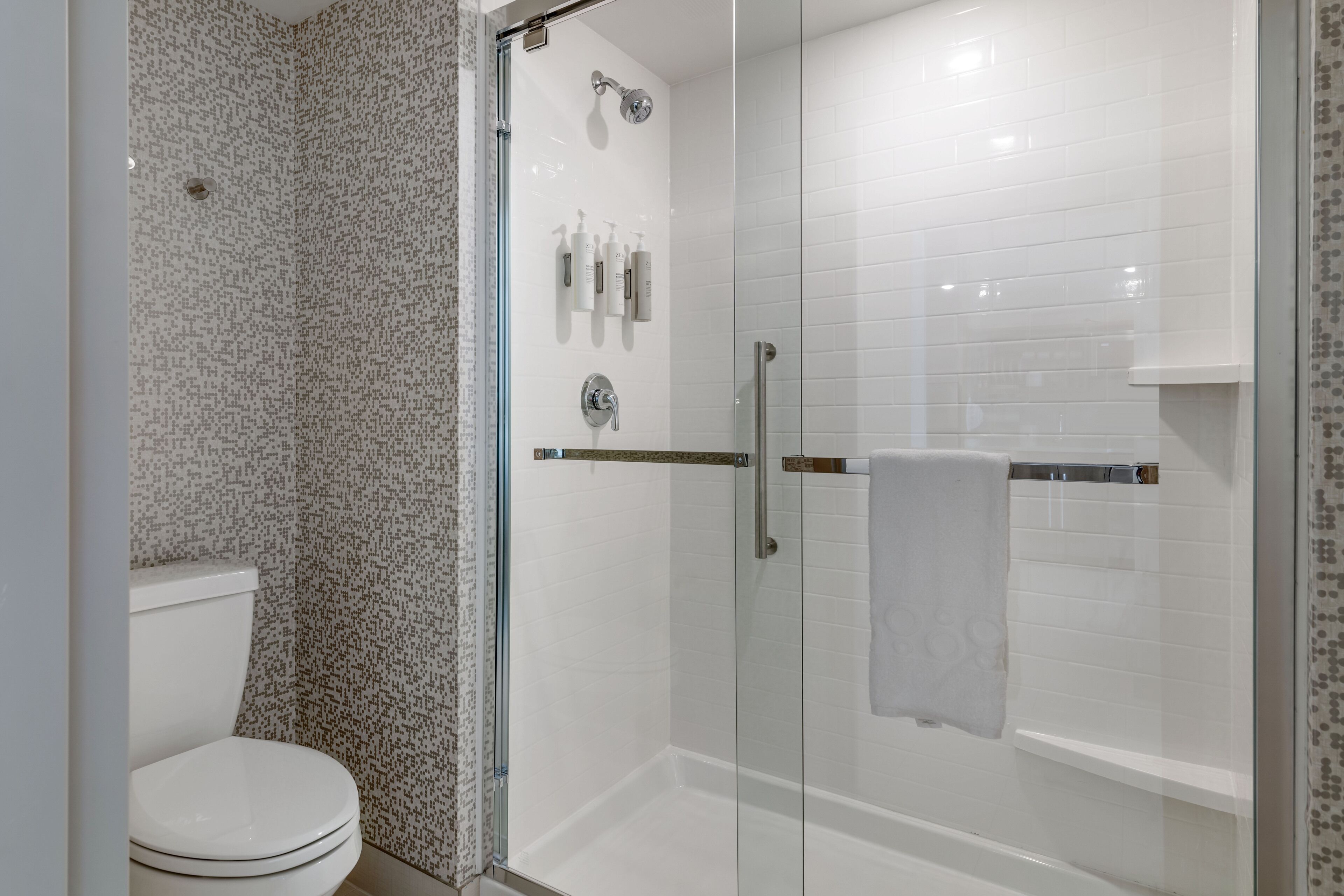 A modern bathroom with a glass-enclosed shower, white tiled walls, and a toilet.