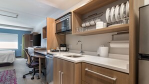 Een moderne keuken met een magnetron, spoelbak en een roestvrijstalen koelkast. Er is een zithoek met een tafel en stoelen, en een bed met een witte spreidek.