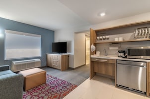 Eine moderne Küche mit integriertem Mikrowellenherd, Backofen und Geschirrspüler. Ein Flachbildfernseher steht auf einem Holzschrank, und es gibt ein Fenster mit Jalousien.