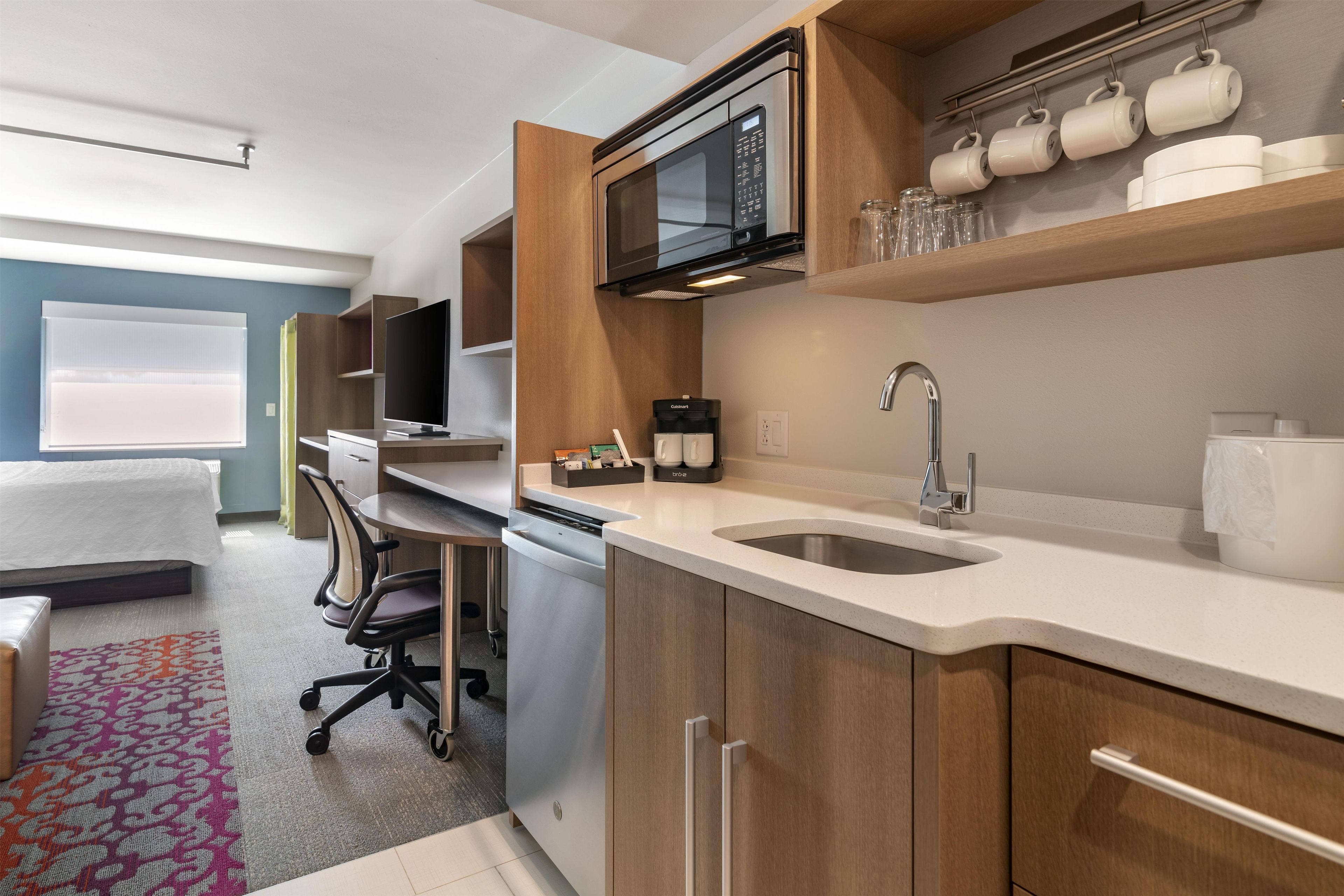 A modern kitchen with a microwave, coffee machine, and a sink. There is a dining area with a table and chairs.