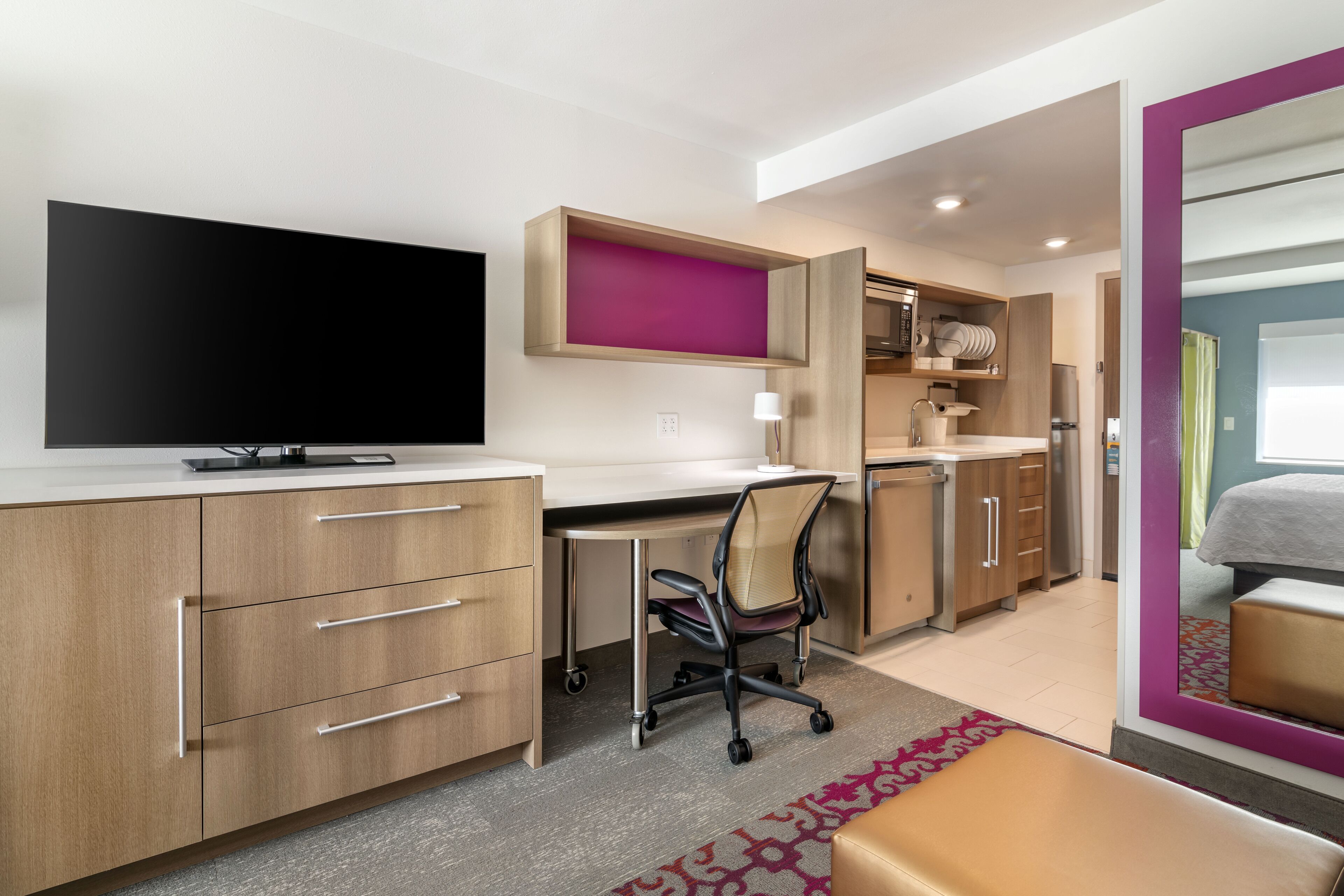 Een moderne hotelkamer met een flatscreen televisie, een bureau met stoel, een bed en een badkamer met douche.