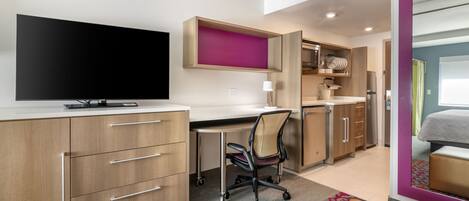 Een moderne hotelkamer met een flatscreen televisie, een bureau met stoel, een bed en een badkamer met douche.