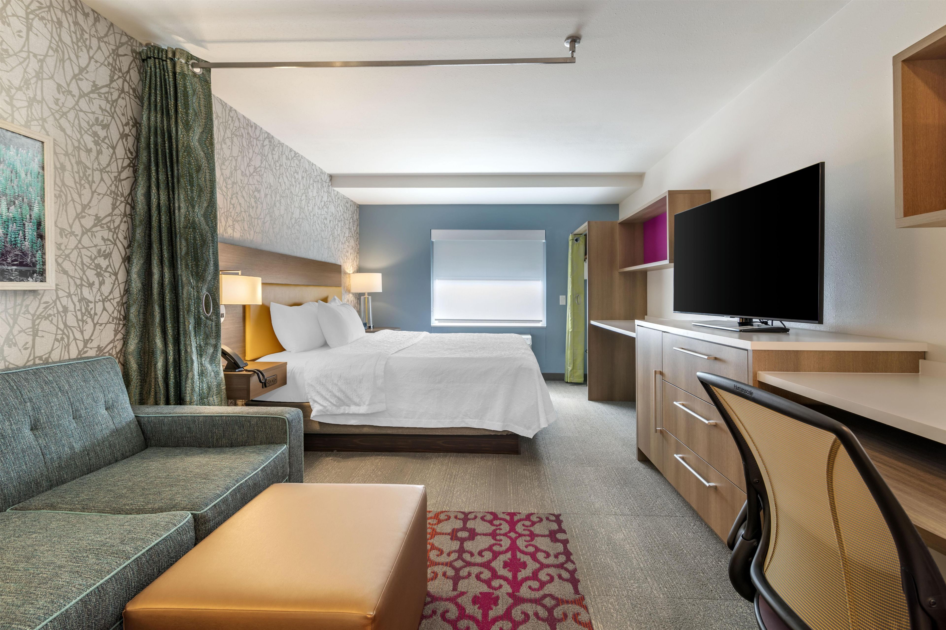 Una camera d'albergo con un letto, un divano, una scrivania, una televisione e una finestra.