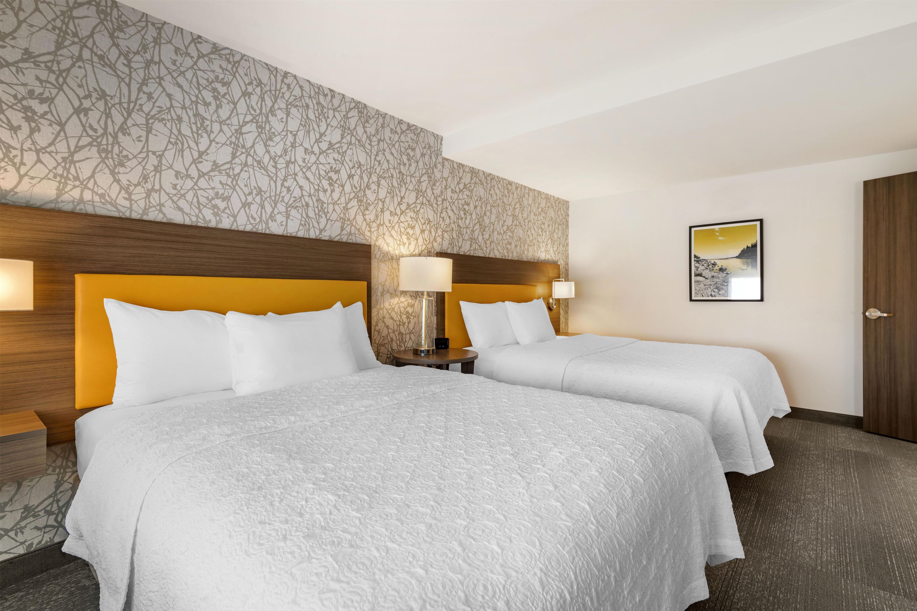Habitació d'hotel amb dos llits, un mur amb dibuixos, un quadre i una porta.
