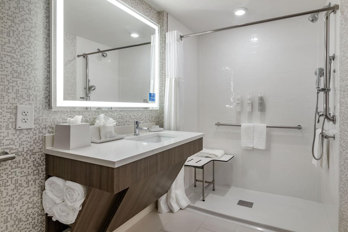 A modern bathroom with a large mirror, two sinks, a shower, and a towel rack.