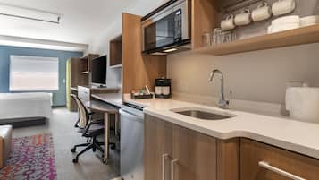 Una cocina moderna con microondas, cafetera y lavabo. Hay un comedor con una silla y una mesa.