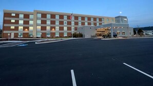 A multi-story hotel with a parking lot in front, featuring a flag and a well-lit entrance. - Home2 Suites by Hilton Bangor (Bangor)