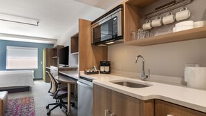 Een moderne keuken met een magnetron, koffiezetapparaat en spoelbak. Er is een eethoek met een tafel en stoelen.