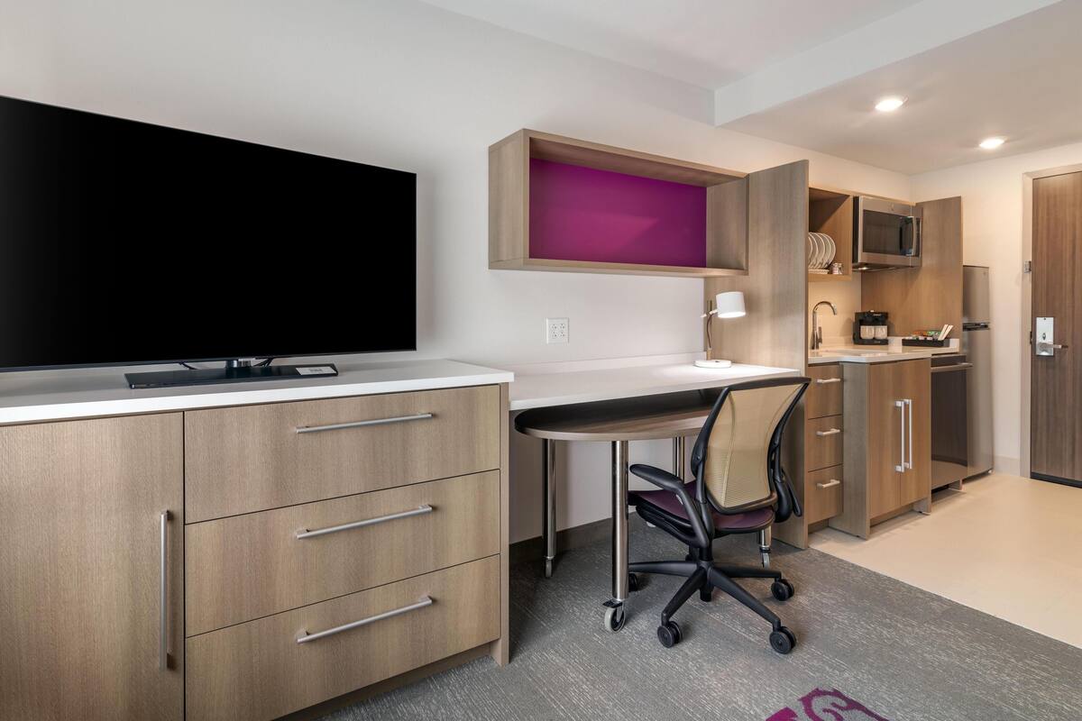 A modern kitchen with a flat-screen TV, wooden cabinets, and a built-in microwave.