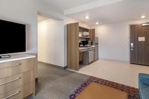 Ein modernes Hotelzimmer mit Flachbildfernseher, einem Holzschrank, einer Küchenzeile und einem gemusterten Teppich.