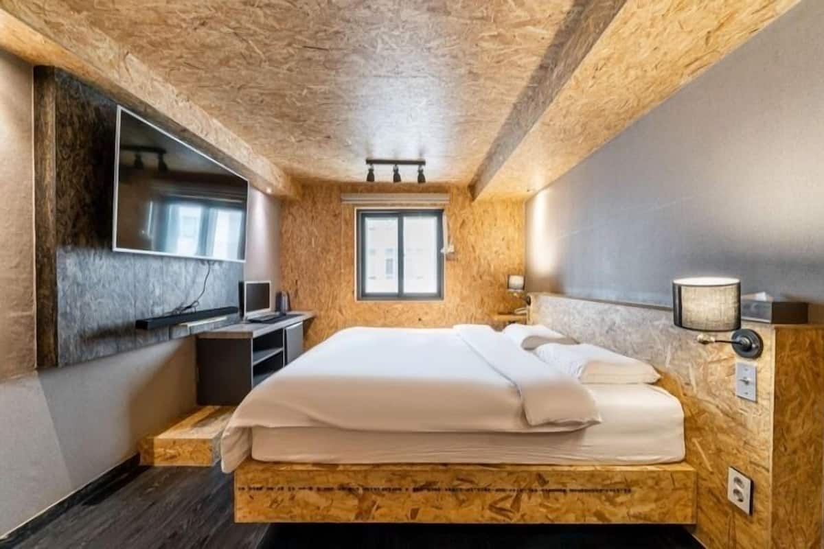 Quarto com cabeceira de madeira, cama, televisão na parede e janela.