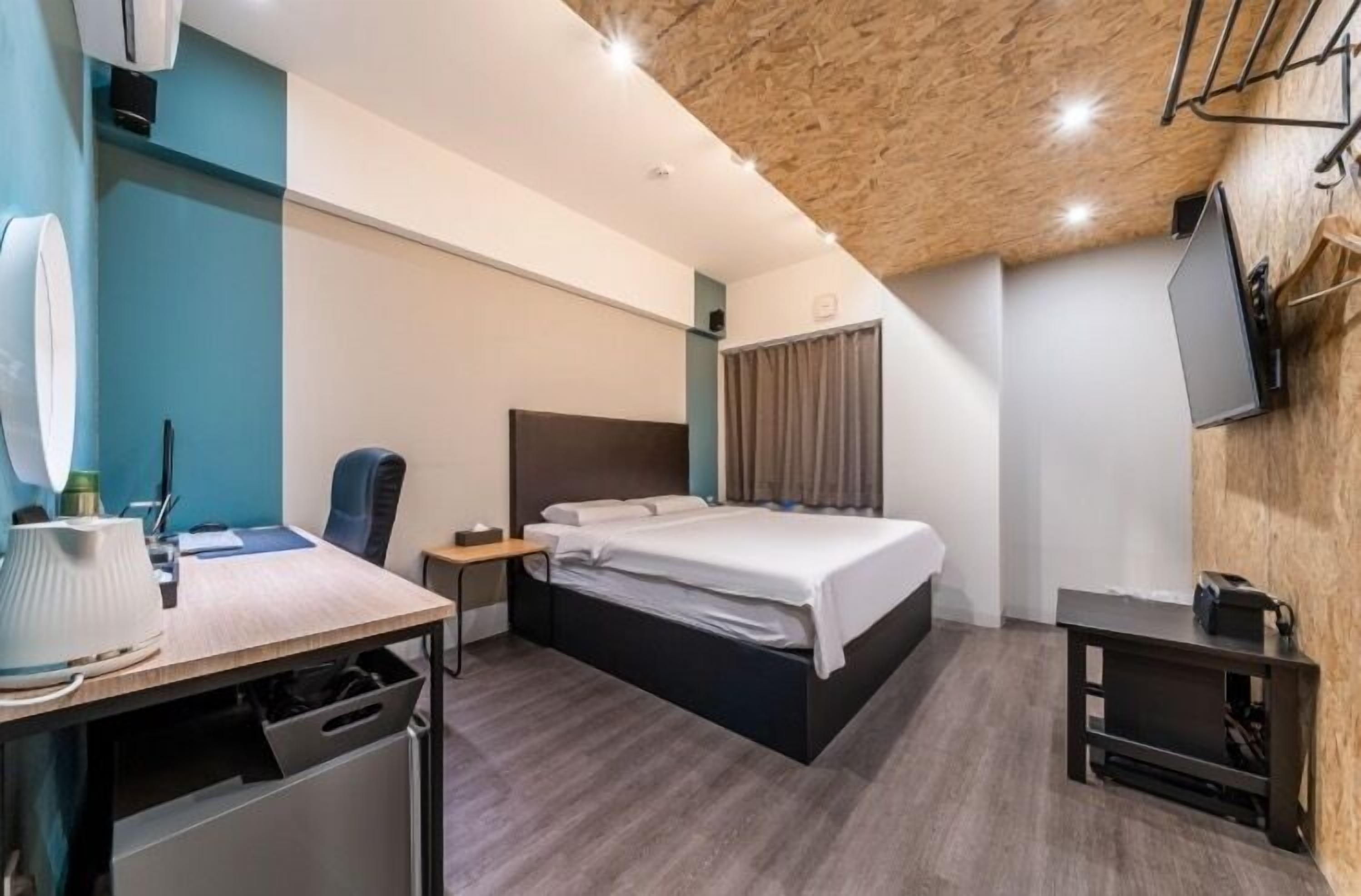 A modern hotel room with a bed, desk, chair, and a TV mounted on the wall.