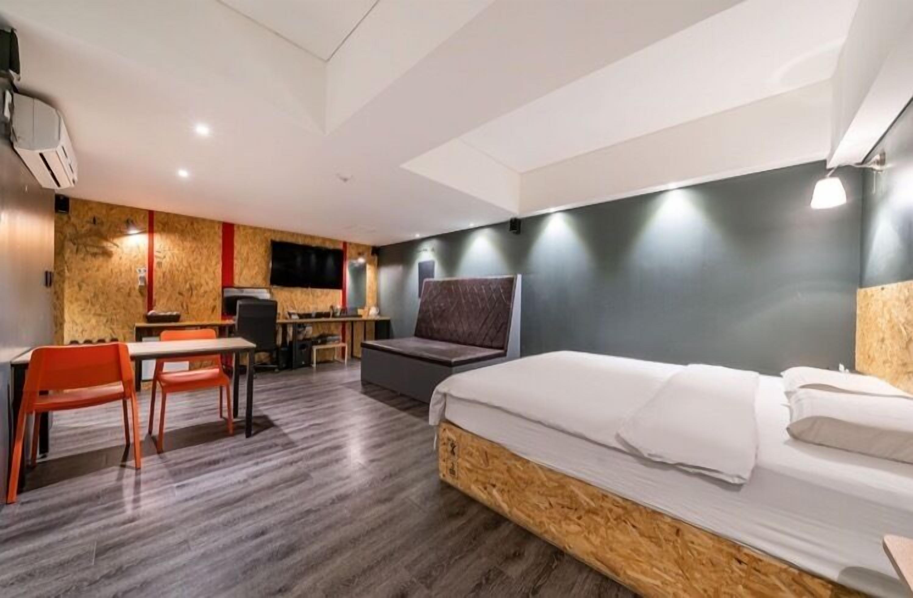 Quarto de hotel com cama, escrivaninha, cadeira e televisão.