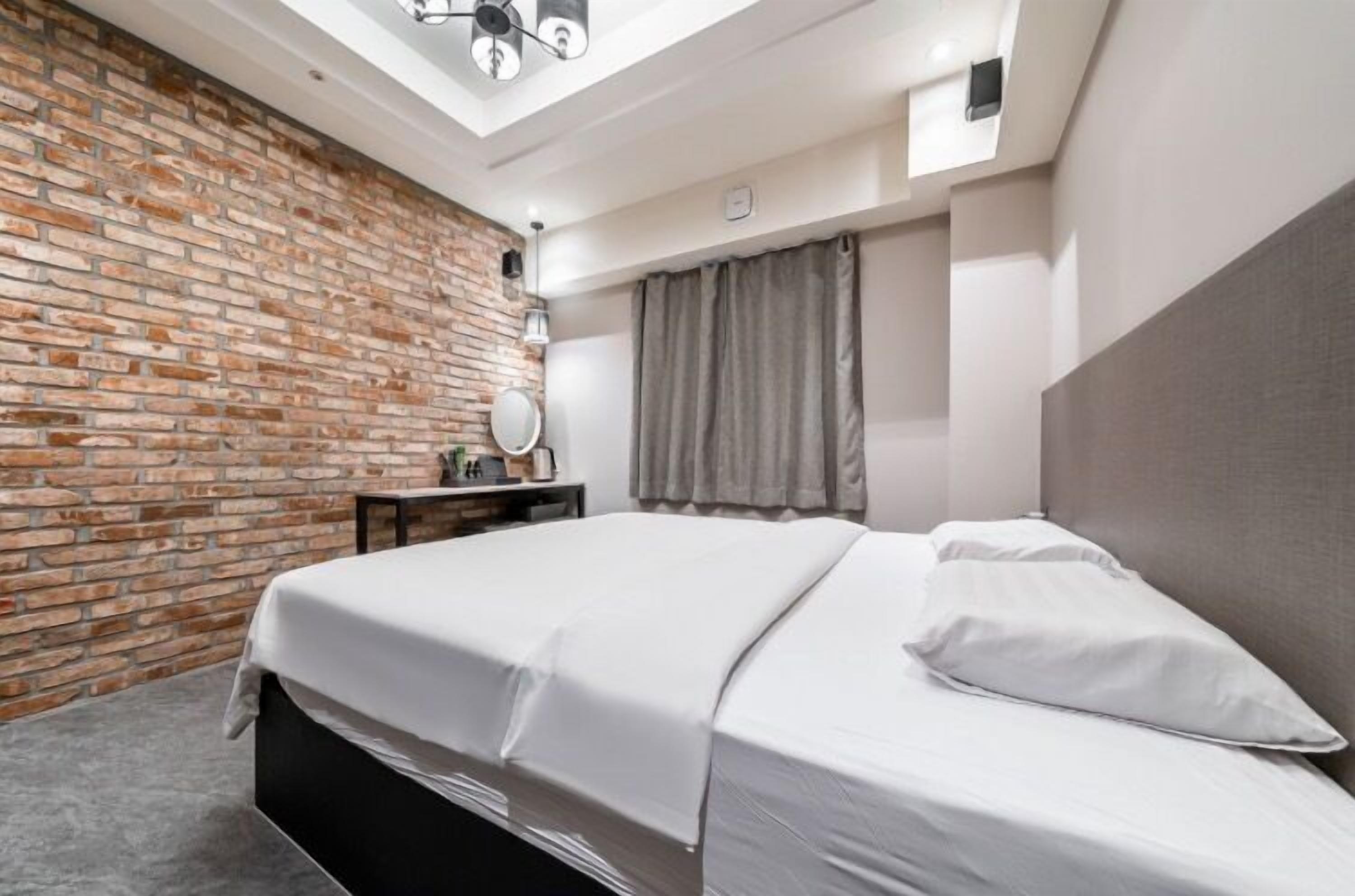 A modern bedroom with a brick wall, a skylight, a bed, a bedside table, and a mirror.