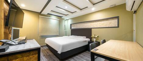 A hotel room with a bed, desk, and chair, a flat-screen TV, a phone, and an air conditioning unit.