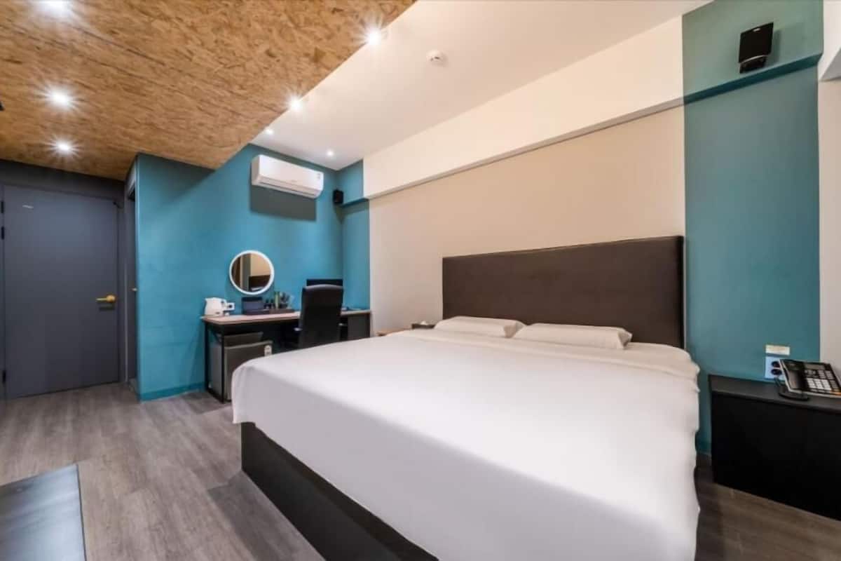 Quarto de hotel moderno com uma cama grande, uma escrivaninha com cadeira, um espelho redondo e um telefone na mesinha de cabeceira.