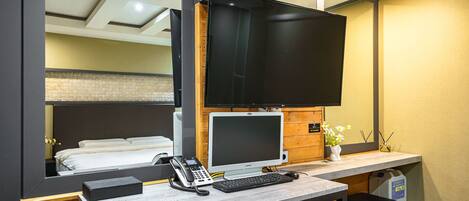 Ein Hotelzimmer mit einem Bett, einem Schreibtisch mit Computer, einem Telefon und einem Fernseher.