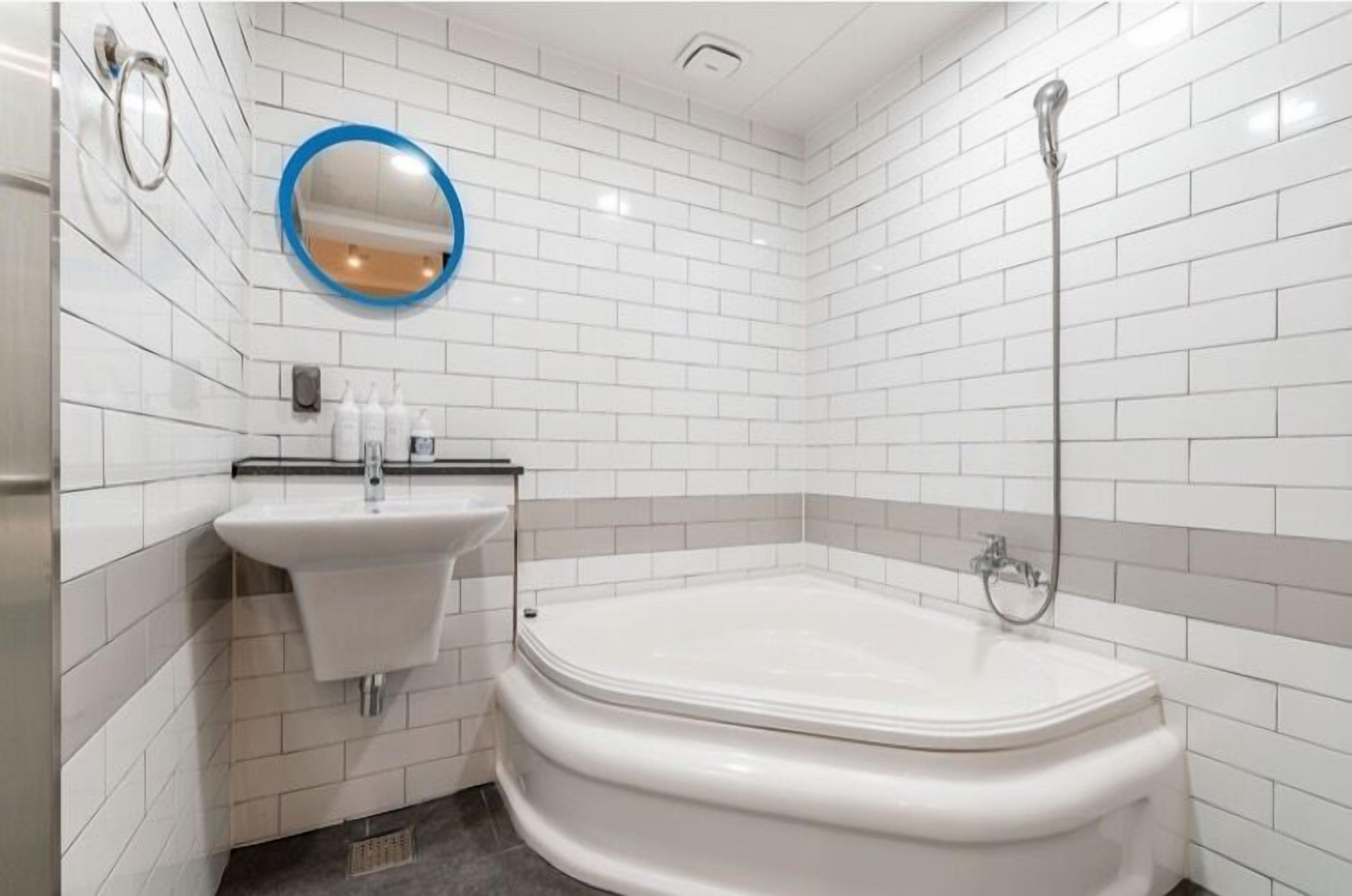 A bathroom with white tiled walls, a white sink with a mirror, and a bathtub.