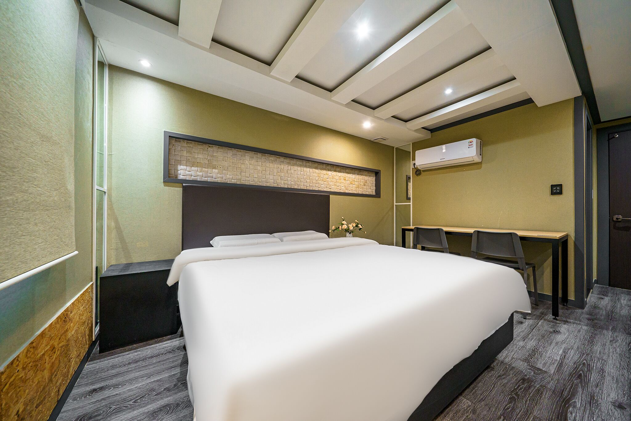 A hotel room with a large bed, a desk, and an air conditioning unit.