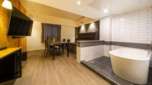 Un baño moderno con una bañera independiente, una mesa de comedor de madera con sillas y un televisor de pantalla plana montado en una pared de madera.