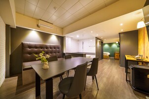 Uma sala de conferências moderna com uma mesa comprida, assentos confortáveis, uma pequena copa e um espaço com chuveiro.