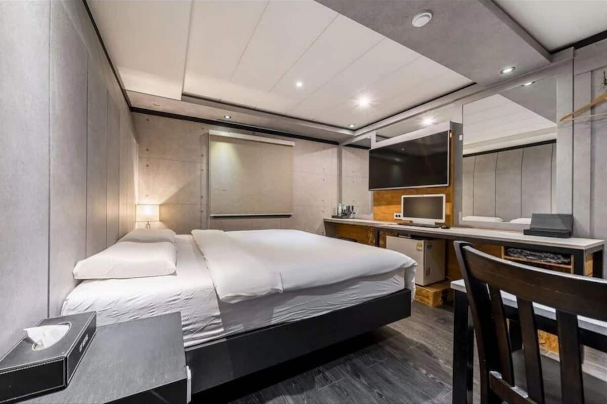 Quarto de hotel moderno com uma cama grande, escrivaninha com computador, espelho e televisão.