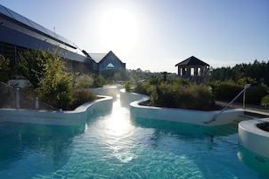 Uma piscina com água cristalina, cercada por vegetação e um gazebo.