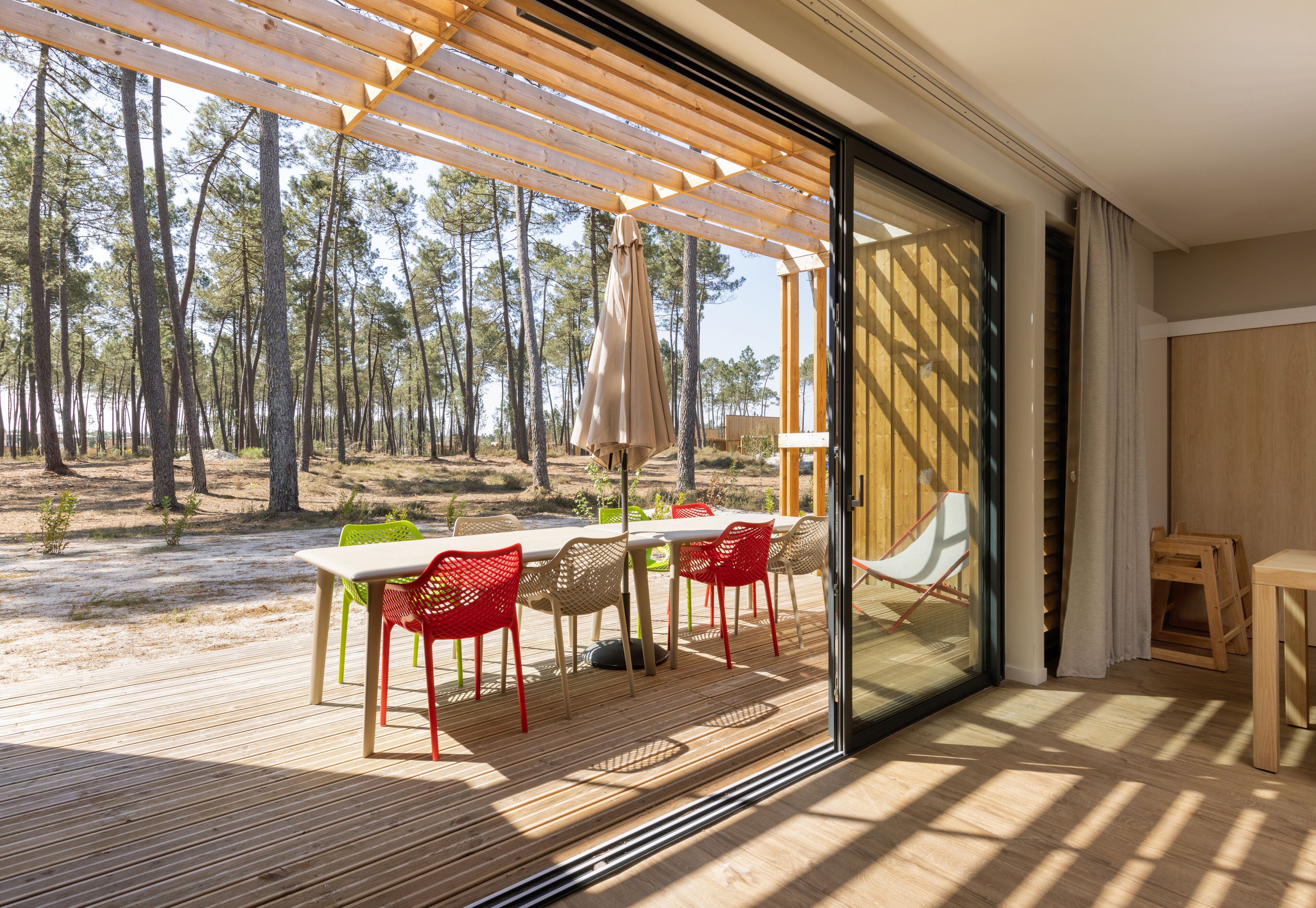 Una terraza exterior con mesa y sillas, un pérgola y vistas a un bosque.
