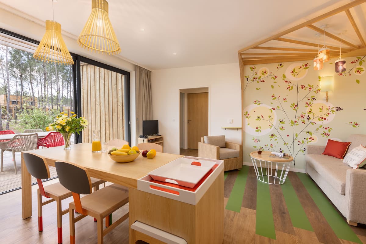 Een moderne woonkamer met een eethoek, houten meubels en een groot raam met uitzicht op bomen.