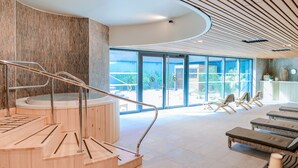 Un espace spa moderne avec des marches en bois menant à un bain à remous, des chaises longues et une vue sur l’extérieur.