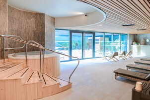 Uma área de spa moderna com escadas de madeira que levam a uma banheira de hidromassagem, cadeiras de descanso e vista para o exterior.