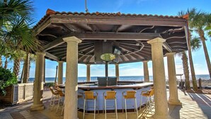 Een overdekt terras met een bar, omgeven door palmbomen en uitzicht op de oceaan.