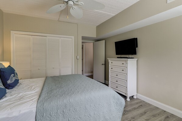 A bedroom with a bed, a dresser, a ceiling fan, and a television.