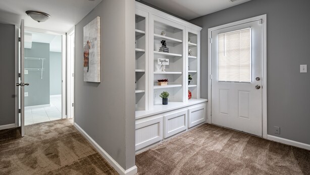 A hallway with a white built-in shelving unit, a door with blinds, and a carpeted floor.