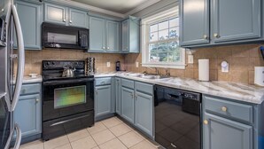 A kitchen with blue cabinets, a stainless steel refrigerator, a black microwave, a stove, and a dishwasher.