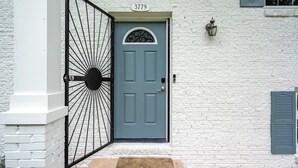 A white brick building with a blue door, a number plate, and a small porch area.