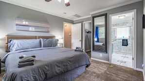A bedroom with a large bed, a ceiling fan, a painting on the wall, and a bathroom with a marble countertop.