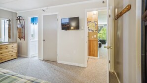 Um quarto com cama, cômoda e televisão fixada na parede.