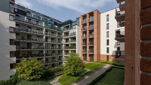 Edifício residencial de vários andares com varandas, um pátio verde e fachada de tijolos.
