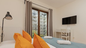 Quarto de hotel com uma cama, escrivaninha, cadeira, televisão e janela com cortinas.