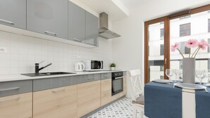 Uma cozinha moderna com armários cinzas e de madeira, micro-ondas, chaleira e um espaço de jantar com mesa posta para dois.